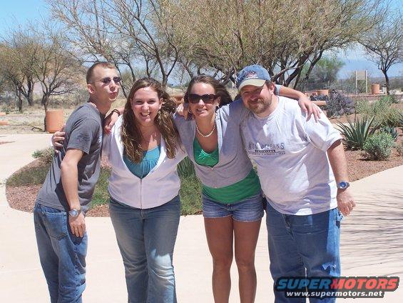 Four people, two men and two women, pose for a photo outdoors with trees and desert plants in the background