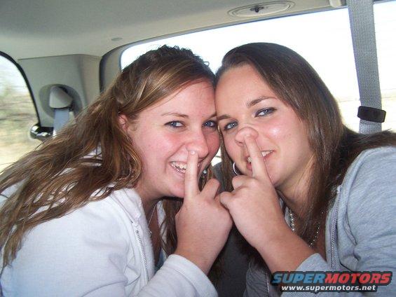 Two women with fingers up their noses inside a vehicle