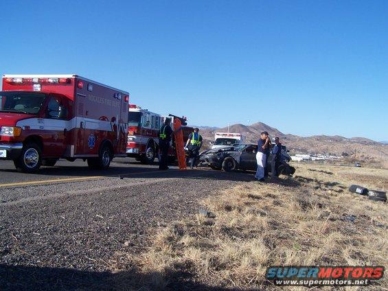 Car accident aftermath with ambulance, fire truck, and damaged car on roadside. People in uniform are present
