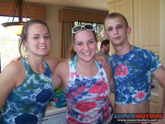 Three smiling people in tie-dye shirts, two women and one man