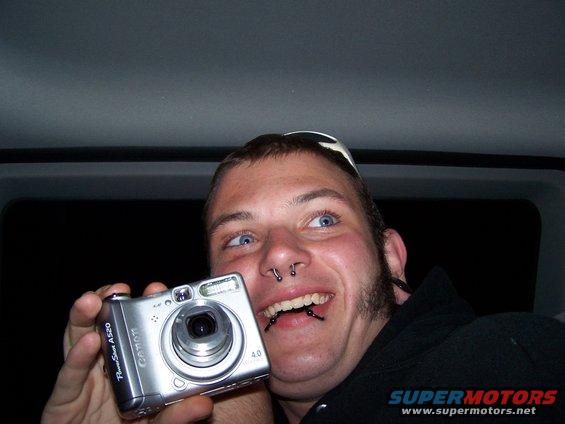 Man with piercings and sunglasses on head holds a silver Canon PowerShot A520 digital camera