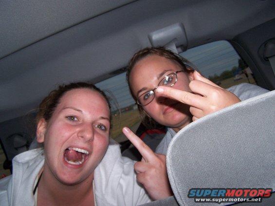 Two young women inside a car, one making a gesture with her fingers