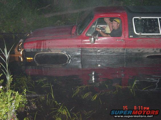 Red and black SUV partially submerged in murky water, with two people inside