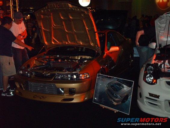 Gold coupe with hood open, front bumper has 'C/M 32' text. A photo of a silver car is displayed in front