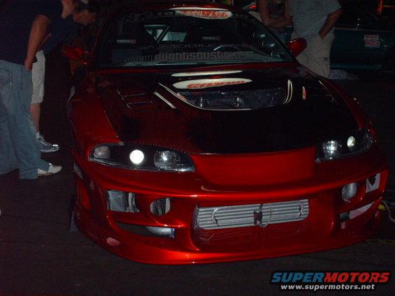 Front view of a red sports car with a custom body kit, aftermarket hood scoop, and intercooler visible