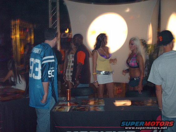 People gathered around tables at an event, some women are standing near a bright light