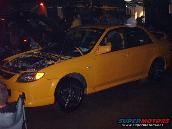 Yellow sedan with hood open, showing engine bay. Aftermarket wheels and body kit visible