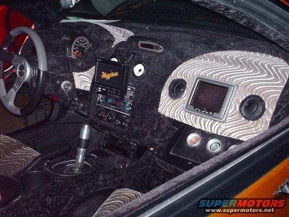 Car interior with fuzzy black dash, aftermarket steering wheel, and two screens. One screen has 'Meguiar's' logo