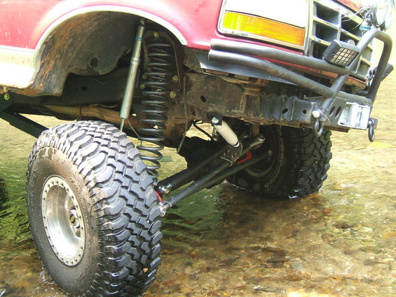Red 1993 Ford Bronco front suspension and large off-road tire in water