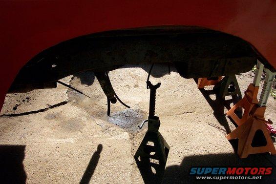 Undercarriage of red vehicle on jack stands, showing frame and suspension components