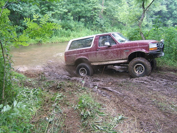 Maroon 1993 Ford Bronco driving through mud and water