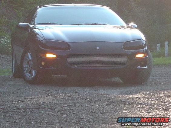 Black Chevrolet Camaro with aftermarket grille, parked on a gravel surface