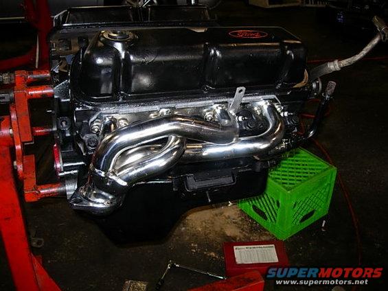 Ford V8 engine with chrome headers, black valve covers, and a red Ford logo