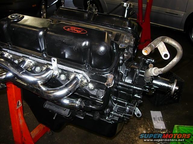 Black Ford engine with chrome exhaust manifold on red stand
