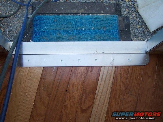 Door threshold with blue mat and hardwood floor. Supermotors.net logo visible