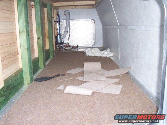 Interior of a camper shell with unfinished wood framing and carpet scraps on the floor