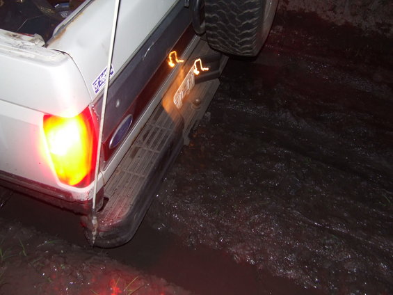 Rear view of a white 1990 Ford Bronco stuck in mud, with its brake lights on