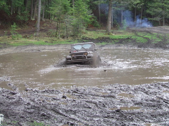 Gray Jeep Wrangler driving through mud puddle, splashing water