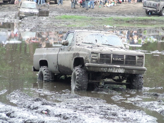 Muddy GMC pickup truck stuck in a mud pit with people watching in the background