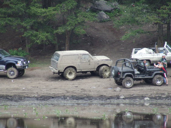 Mud-covered beige SUV, 3/4 front view, with large tires and visible damage to the hood