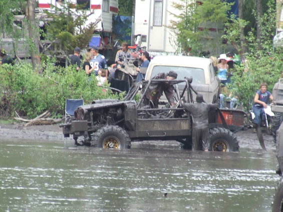 Muddy off-road vehicles in water with people around