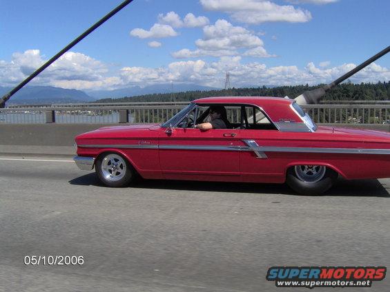 Side view of a red 1964 Ford Fairlane driving on a bridge