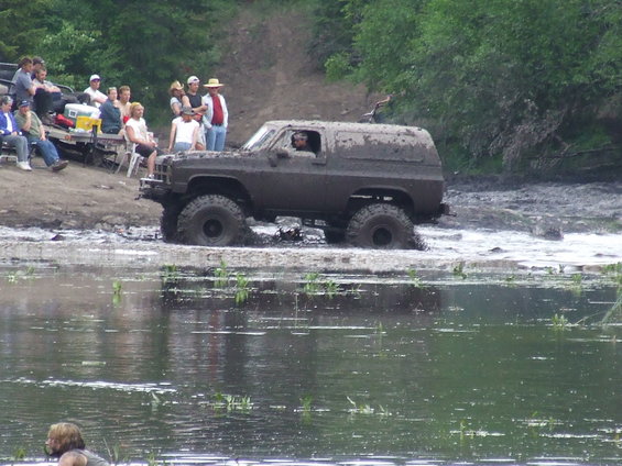 Muddy off-road SUV driving through water with people watching on the bank