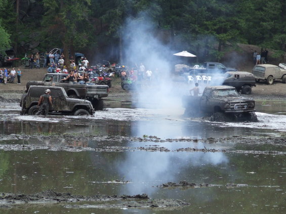 Muddy off-road trucks and SUVs participating in a bogging event with spectators watching