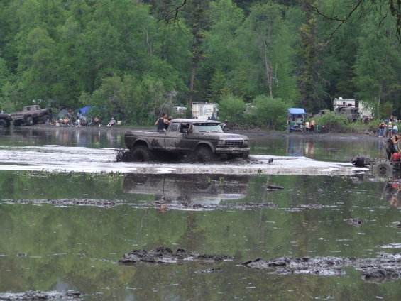 Brown pickup truck driving through mud, 3q-front view