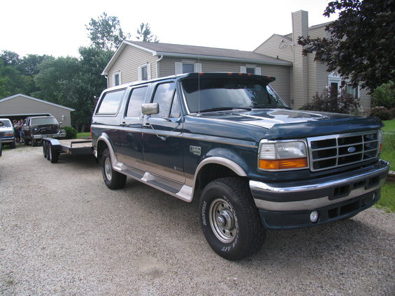 Dark teal Ford Bronco Centurion conversion with tan trim, towing a trailer. Front 3/4 view