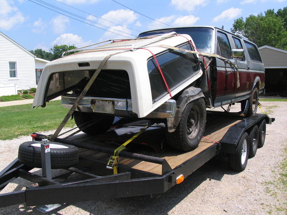1987 Ford Bronco with its top removed, strapped to a trailer. The body is two-tone red and gray