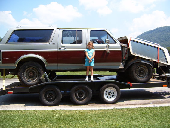Two-tone silver and maroon SUV on a trailer, with a young girl standing in front of it