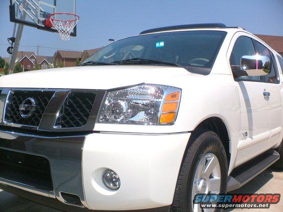 White Nissan Armada SUV front 3/4 view, chrome grille, headlights, and bumper accents. Basketball hoop in background