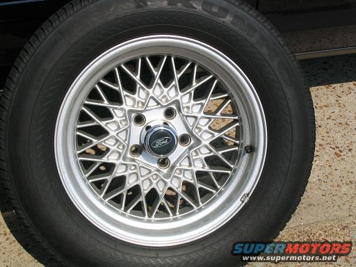 Close-up of a silver wire-spoke wheel with a black tire and a Ford center cap