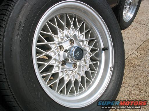 Close-up of a silver mesh wheel with a Ford logo center cap and a tire. Another wheel is visible in the background