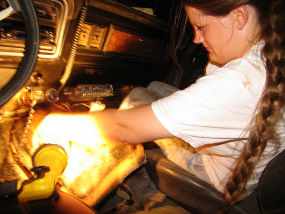 Person working on vehicle transmission tunnel with yellow flashlight