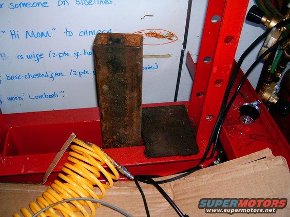 Rusty metal block on red stand with yellow air hose and whiteboard in background