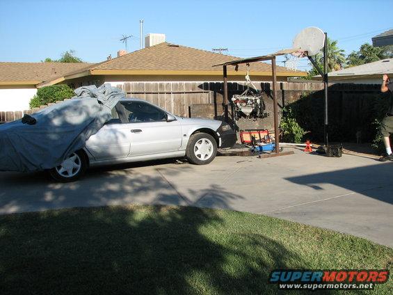 Silver sedan with car cover on rear half, engine hoist lifting engine out of bay