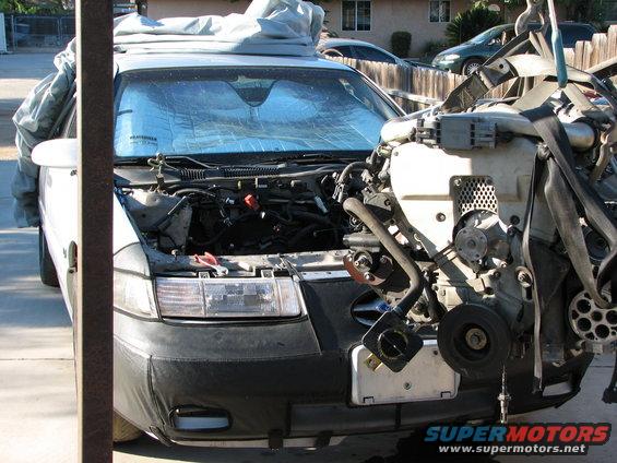 Car with hood open, engine being lifted out by a hoist. Sunshade on windshield