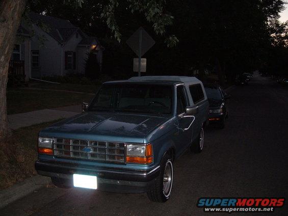 Blue Ford Bronco II parked on street, another car behind it