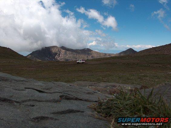 White pickup truck drives across a grassy plain with mountains in the background