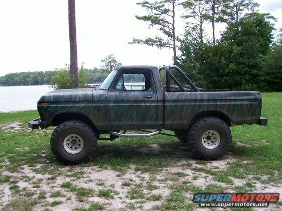 1979 Ford pickup truck with camouflage paint and roll bar, parked by a lake