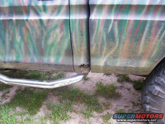 Side of a truck with camouflage paint and a chrome step bar. There's rust on the lower body panel