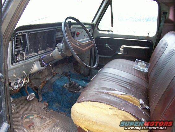 Interior of a worn truck with blue carpet and torn brown seat. Floor mat shows 'FORD'