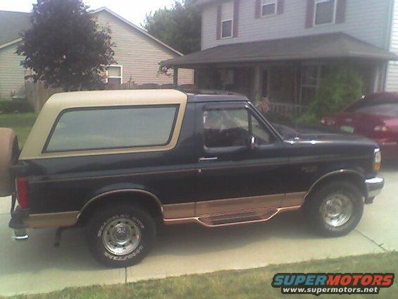 Dark blue Ford Bronco with tan top and woodgrain trim, side view, spare tire on rear