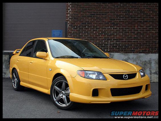 Yellow sedan parked in front of a brick building. It has a spoiler and aftermarket wheels