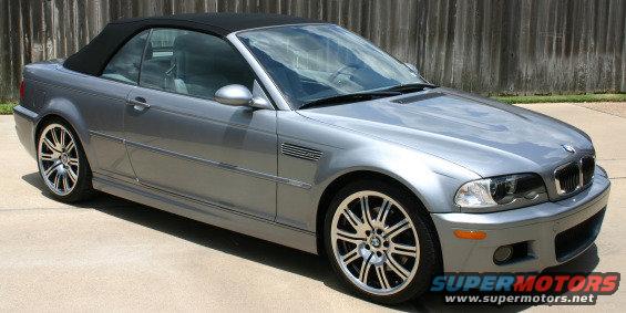 Silver BMW M3 convertible with black top parked on concrete, wooden fence behind