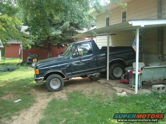 Dark green pickup truck parked under a carport, angled view from the front