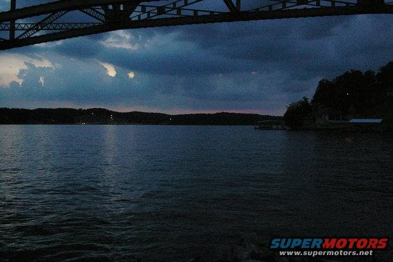 Lake scene under a bridge at dusk with Supermotors logo
