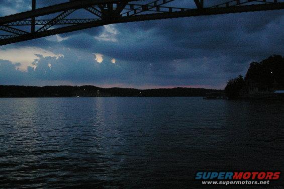 Lake and bridge structure at dusk with dark clouds overhead